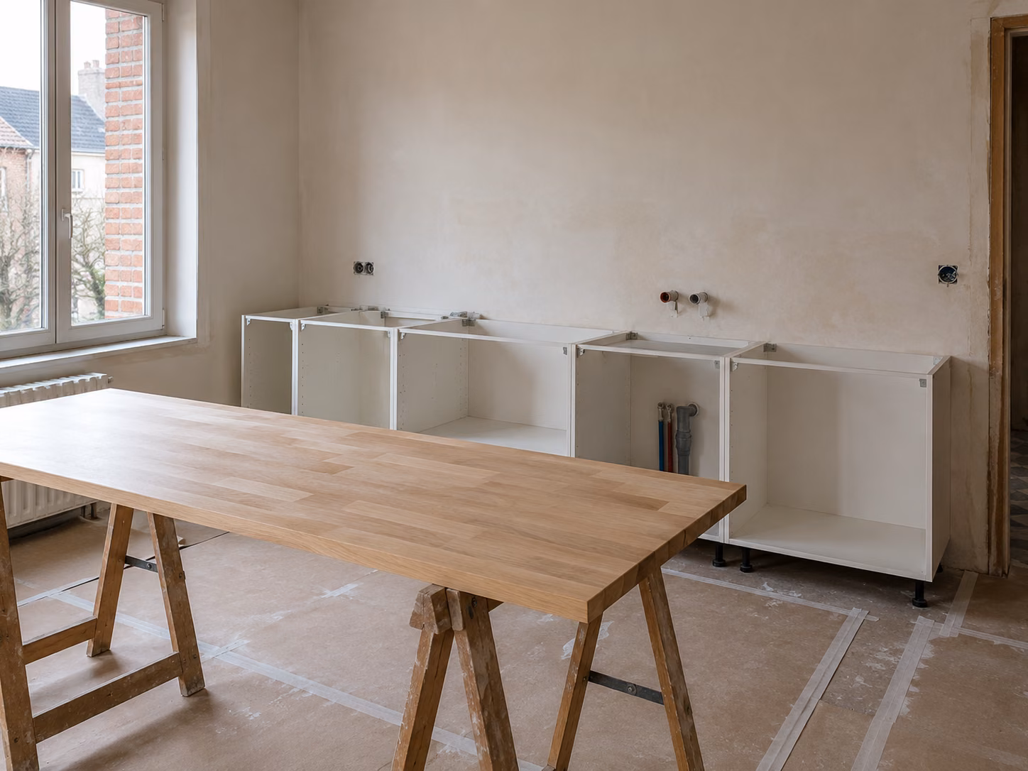 Cuisine en cours de pose, caissons bas alignés sans façades et plan de travail en bois posé sur tréteaux